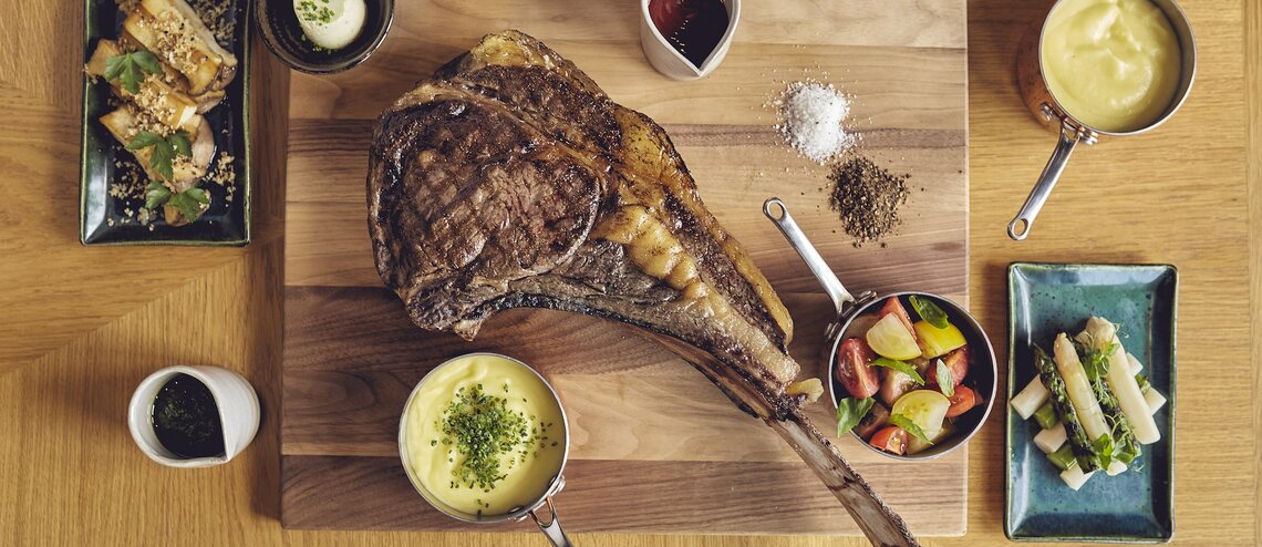 Elegantes Steakgericht mit Beilagen auf Holzbrett, serviert im LOUIS Hotel München.