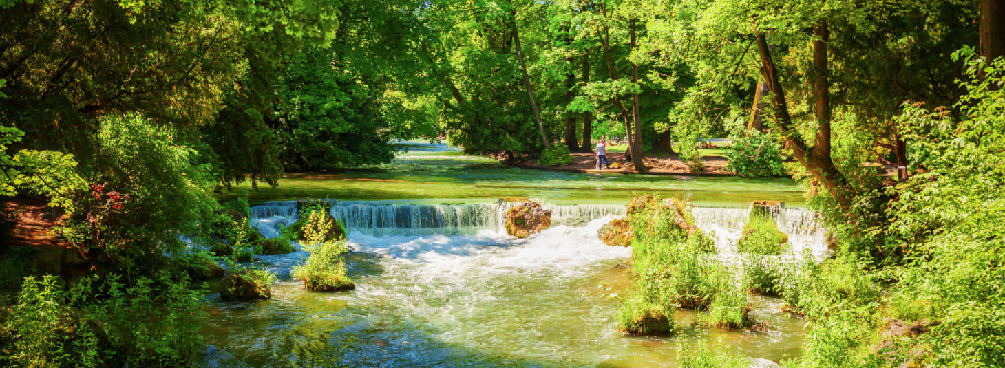 Kleiner Wasserfall im Englischen Garten München, umgeben von üppigem Grün und Bäumen.