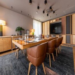 Moderner Konferenzraum im LOUIS Hotel München mit großem Holztisch, Lederstühlen und Flachbildschirm.