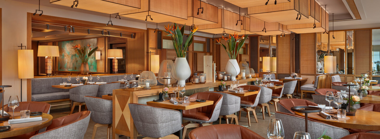 Elegantes Restaurant im LOUIS Hotel München mit stilvollen Holztischen, gemütlichen Sesseln und warmem Lichtambiente.