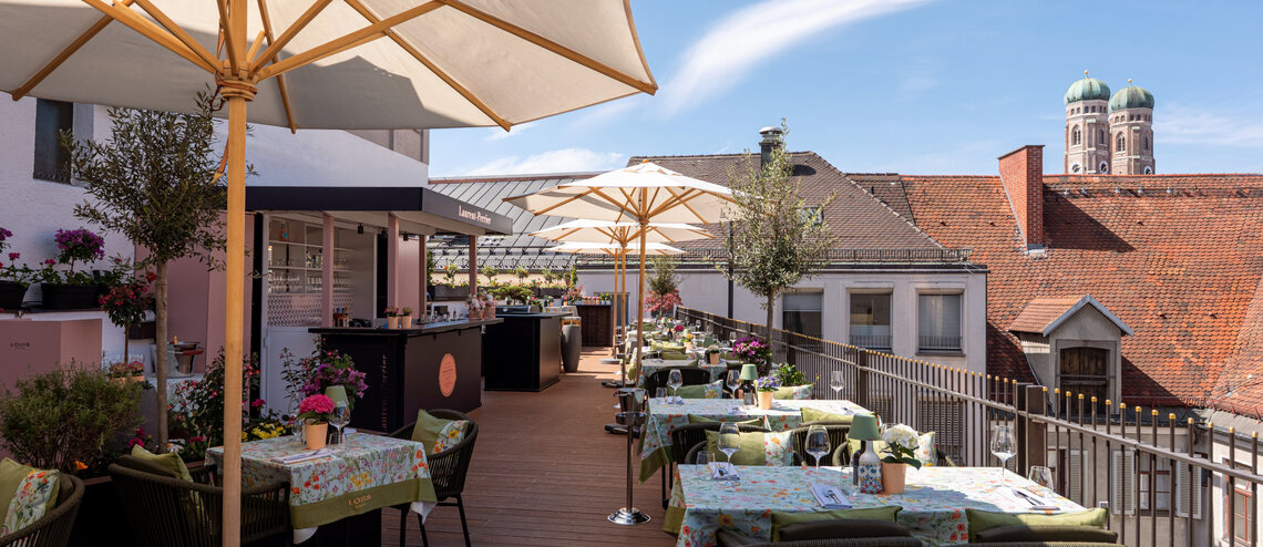 Die Dachterrasse mit Sonnenschirmen, vielen bunten Sitzgruppen und Blick auf die Frauenkirche.