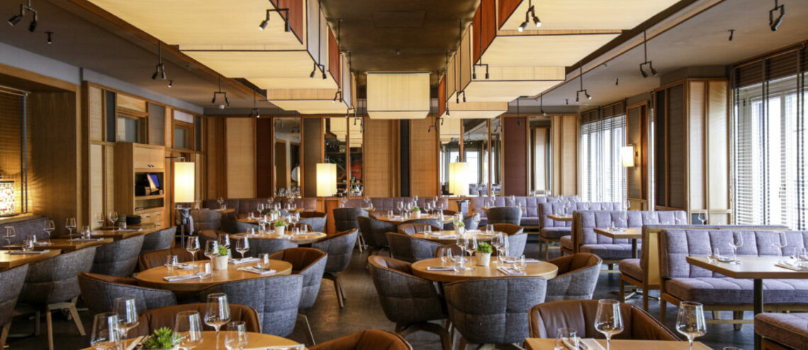 Modernes Restaurant im LOUIS Hotel München mit stilvollen Holztischen, gedeckt mit Gläsern und Besteck, gemütliche Sitzgelegenheiten.