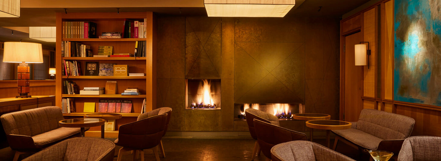 Gemütliche Hotel-Lounge mit Sesseln, Kamin, Bücherregal und stimmungsvoller Beleuchtung im LOUIS Hotel München.