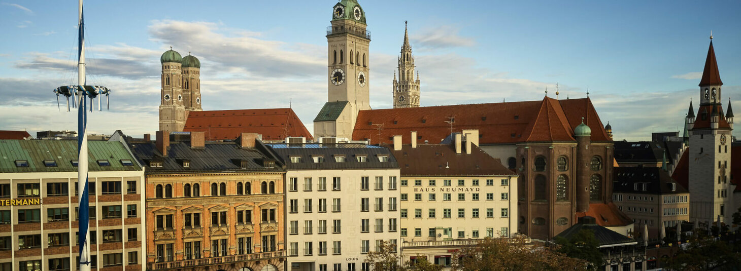 Blick auf Münchens Altstadt mit historischen Gebäuden, Kirchtürmen und einem Maibaum bei blauem Himmel.