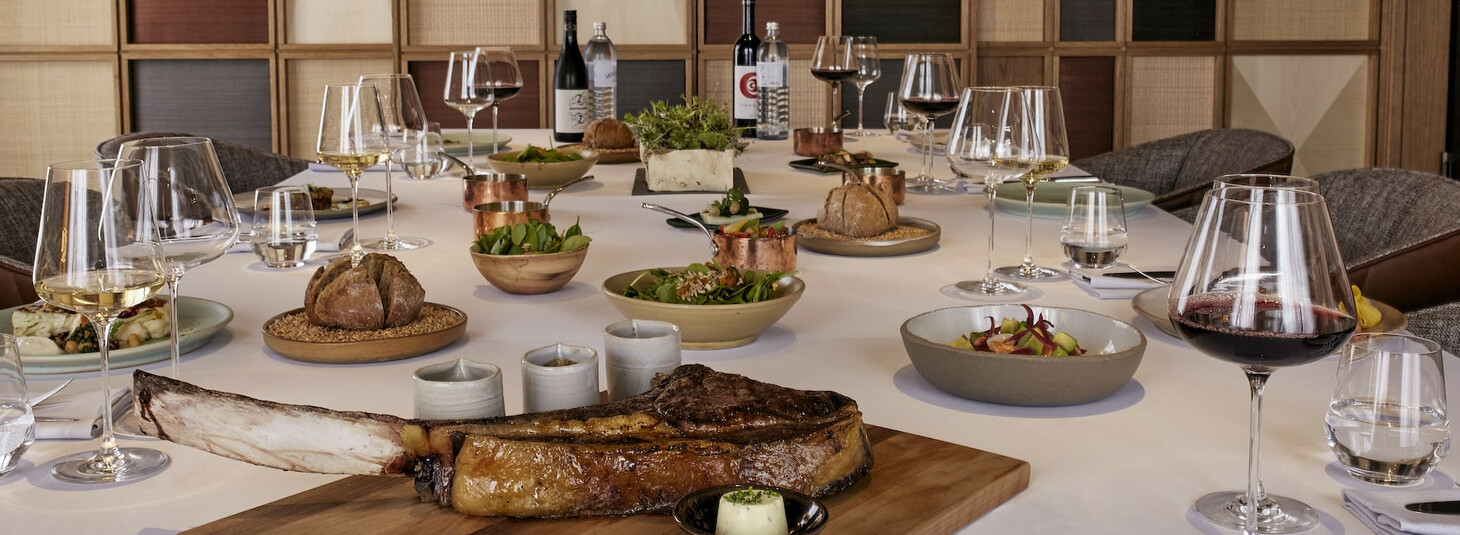 Eleganter, gedeckter Tisch im LOUIS Hotel München mit Wein, Salaten und Fleischgericht.