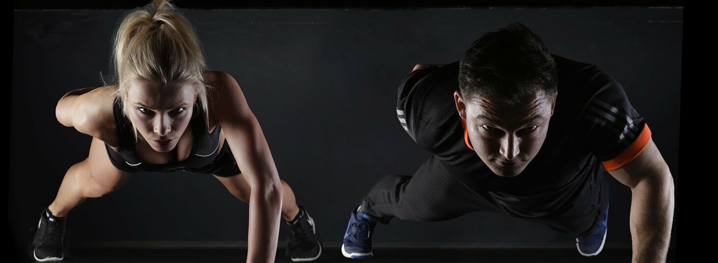 Zwei Personen machen Liegestütze in einem Fitnessstudio, frontal aus der Vogelperspektive fotografiert.