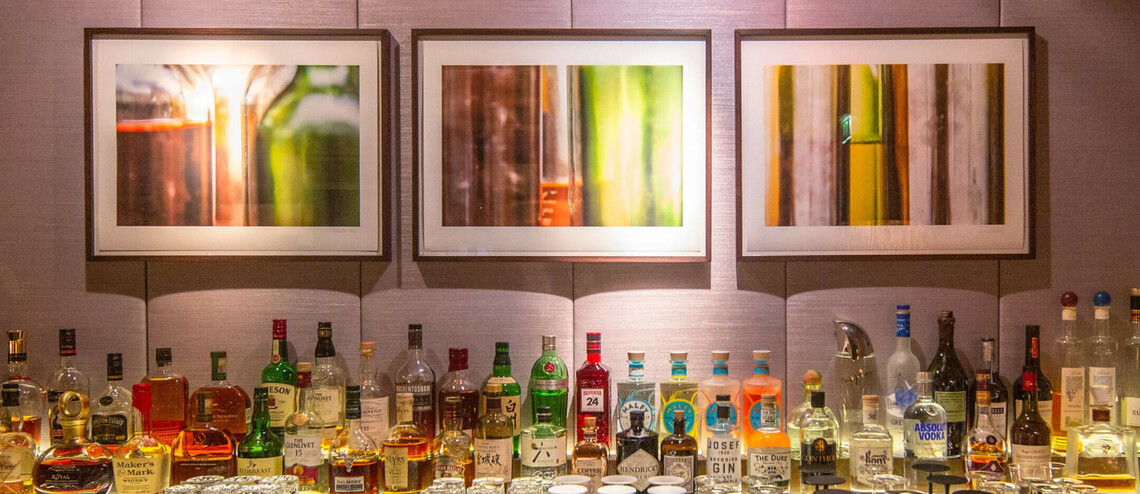Hotelbar mit verschiedenen Spirituosenflaschen und Gläsern vor drei abstrakten Wandbildern.