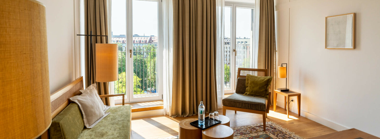 Helles Hotelzimmer mit modernen Möbeln, großen Fenstern und Blick auf die Stadt im LOUIS Hotel München.