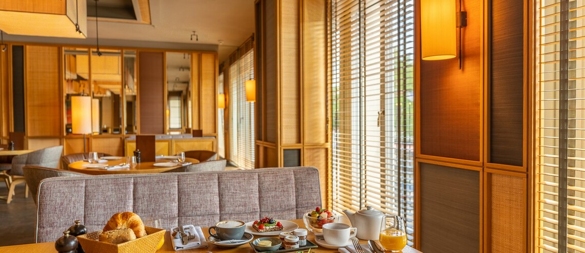 Gemütliches Hotelrestaurant mit gedecktem Frühstückstisch, Holzmöbeln und warmem Licht.