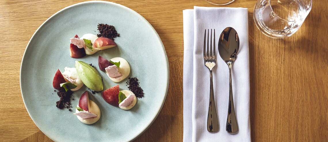 Elegantes Dessert auf blauem Teller mit Besteck und Gläsern auf Holztisch im LOUIS Hotel München.