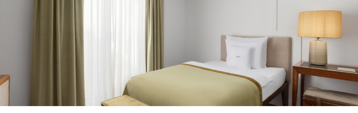 A cosy hotel room with a single bed, a green bedspread and warm lighting.