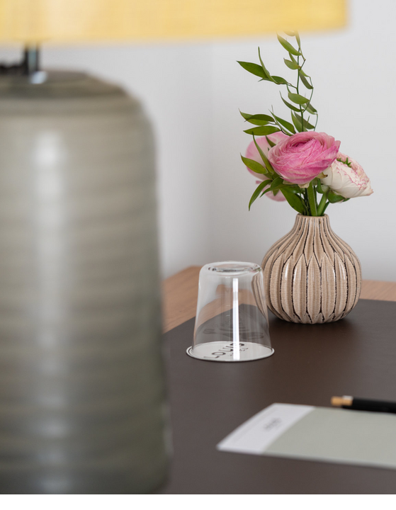 Bedside table with a vase of flowers, a glass of water and a notepad.