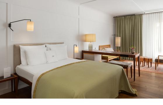 Comfortable hotel room with double bed, desk, armchairs and large windows with curtains at the LOUIS Hotel Munich.