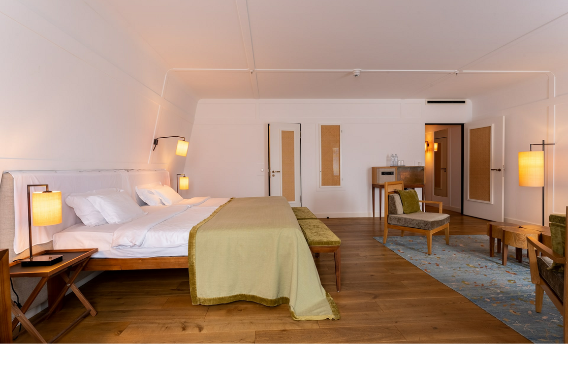 Helles, modernes Hotelzimmer mit großem Bett, Holzboden, stilvollen Lampen und Sitzbereich im LOUIS Hotel München.