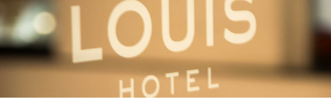 Lettering "LOUIS HOTEL" on glass, blurred background.