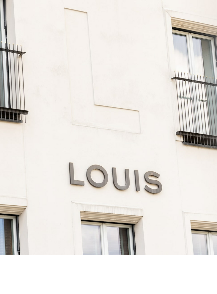 Fassade des LOUIS Hotels in München mit großen Fenstern und Balkongittern.