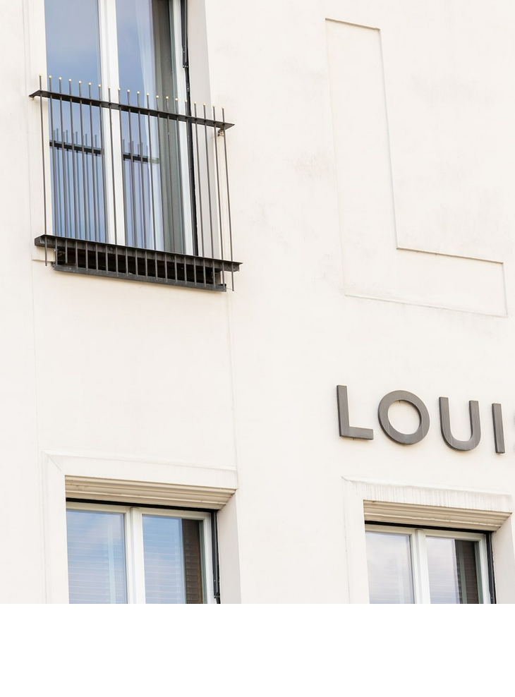Façade of the LOUIS Hotel in Munich with large windows and balcony grilles.