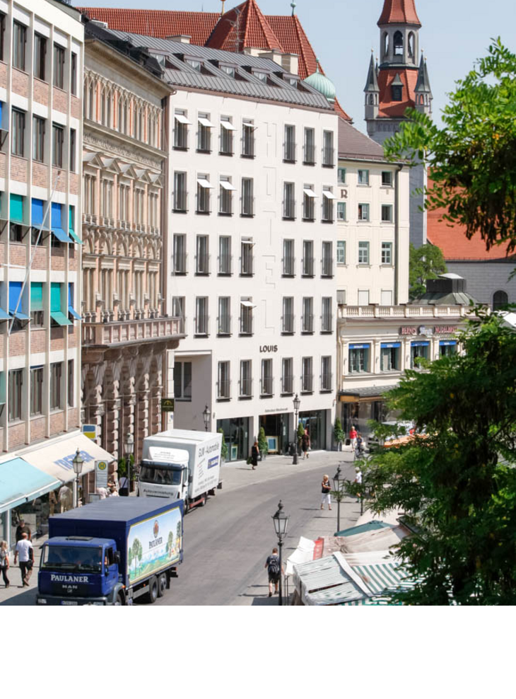 Exterior view LOUIS Hotel Munich Viktualienmarkt LOUIS Hotel in Munich, modern building in urban surroundings, with market stalls and church tower in the background.