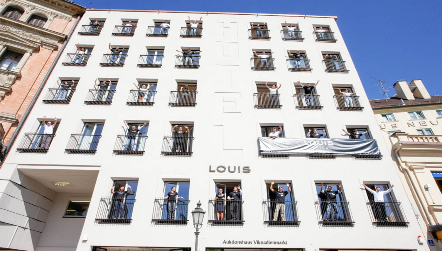 Fassade des LOUIS Hotels in München mit Menschen auf Balkonen, die freundlich winken.