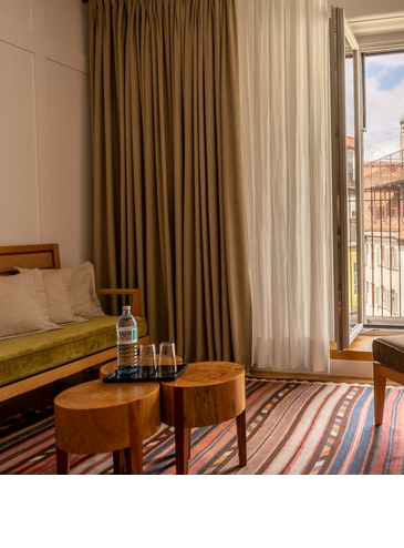 Gemütliches Hotelzimmer mit offener Balkontür und Blick auf die Türme der Frauenkirche in München.