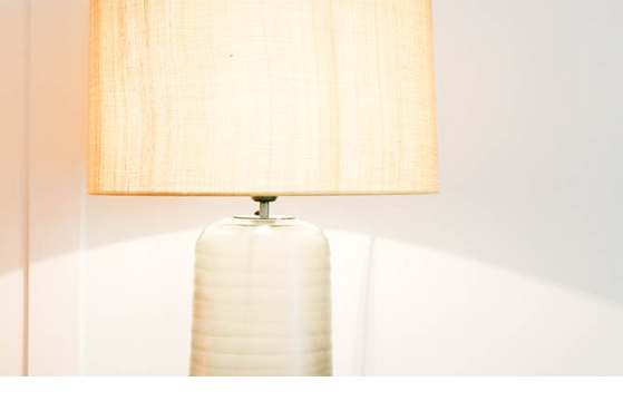 Table lamp with bright shade on wooden table, next to it a telephone and information card in the LOUIS Hotel Munich.