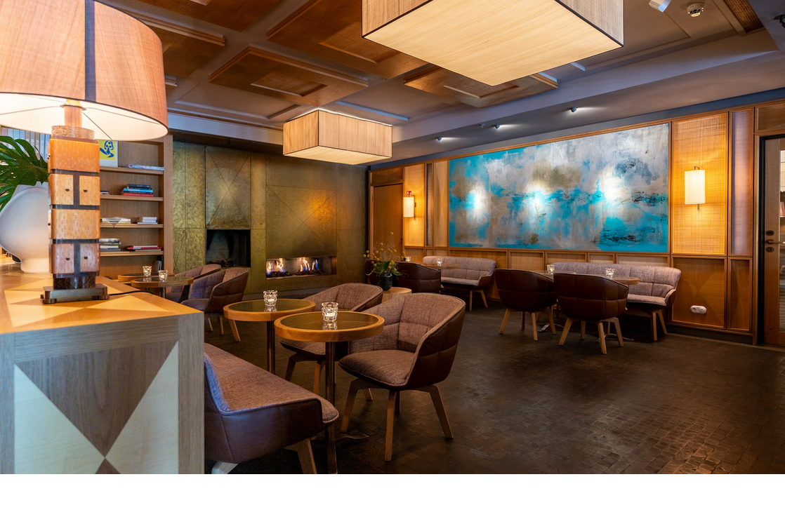 Elegant hotel lounge with modern armchairs, wooden tables, fireplace and large, abstract wall painting in shades of blue and brown.