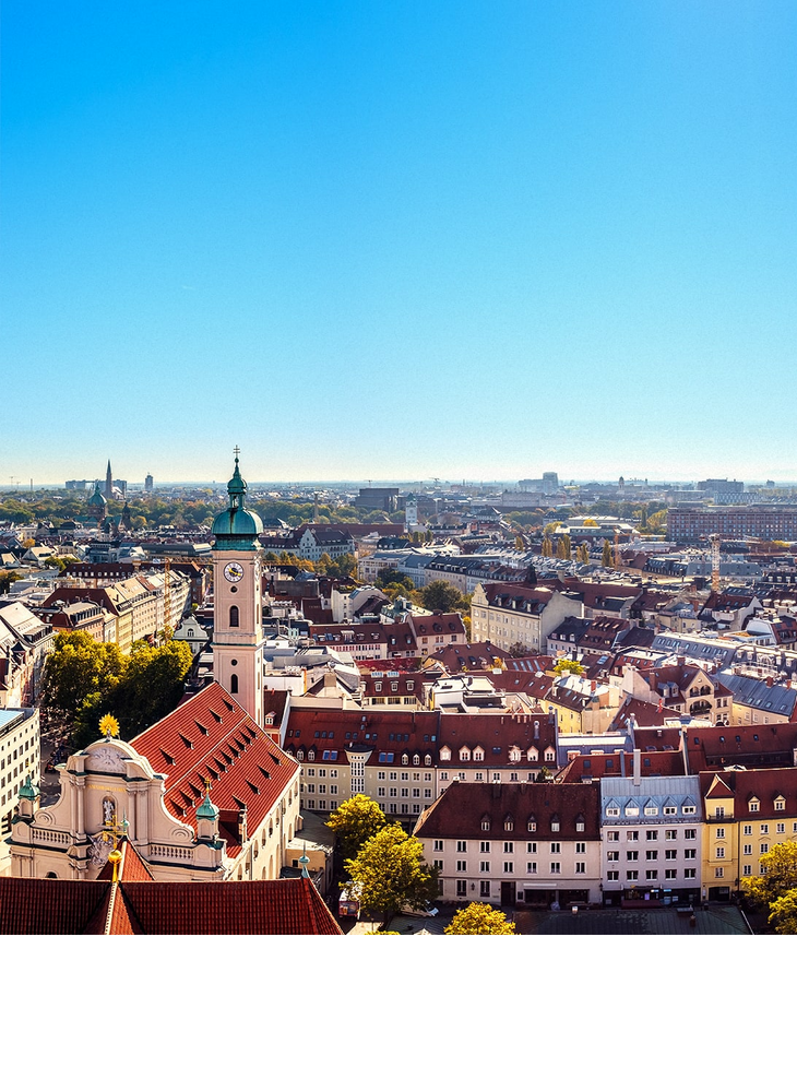 Stadtansicht von München bei klarem Himmel, mit Kirchturm und bunten Gebäuden im Vordergrund.