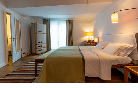 Modernes Hotelzimmer mit großem Bett, Holzfußboden, stilvoller Beleuchtung, Kleiderschrank und Schreibtisch am Fenster.