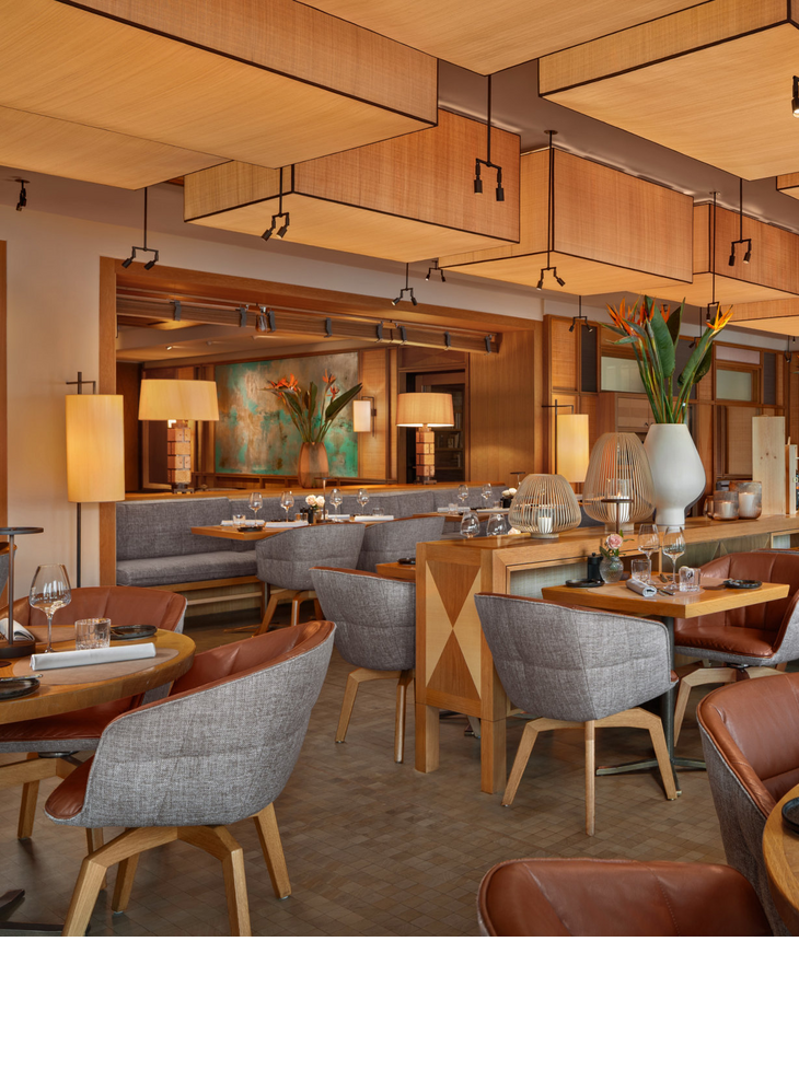 Elegant restaurant in the LOUIS Hotel Munich with stylish wooden tables, cozy armchairs and a warm lighting ambience.