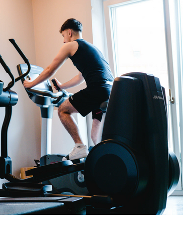 Ein Mann trainiert auf einem Heimtrainer im Fitnessraum des LOUIS Hotel München.