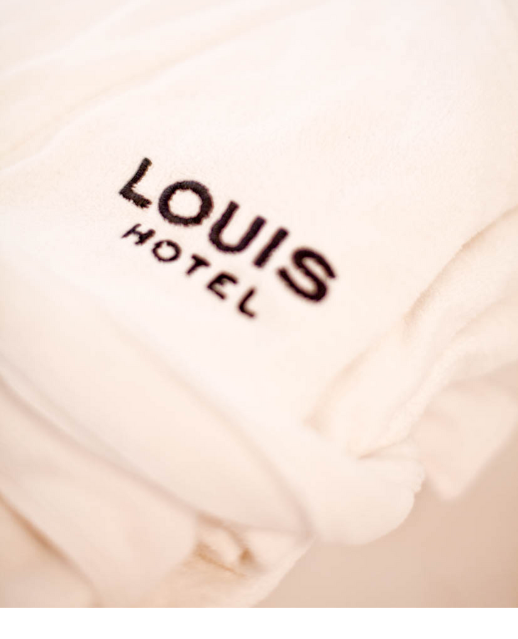 White hotel bathrobe with black LOUIS Hotel logo, soft and luxurious.