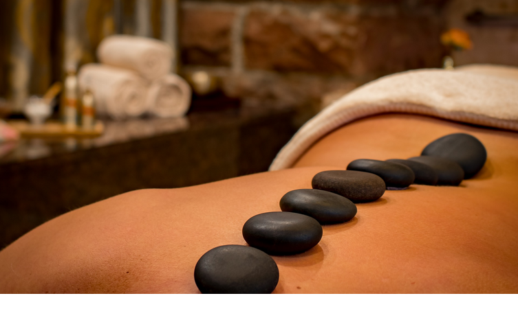 Person during a hot stone massage at the LOUIS Hotel Munich, with dark stones on the back.