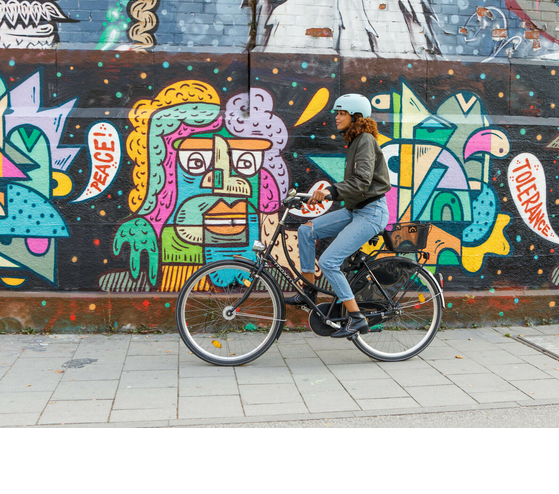 Person on a bicycle in front of a colorful graffiti wall with the words "Peace" and "Tolerance".
