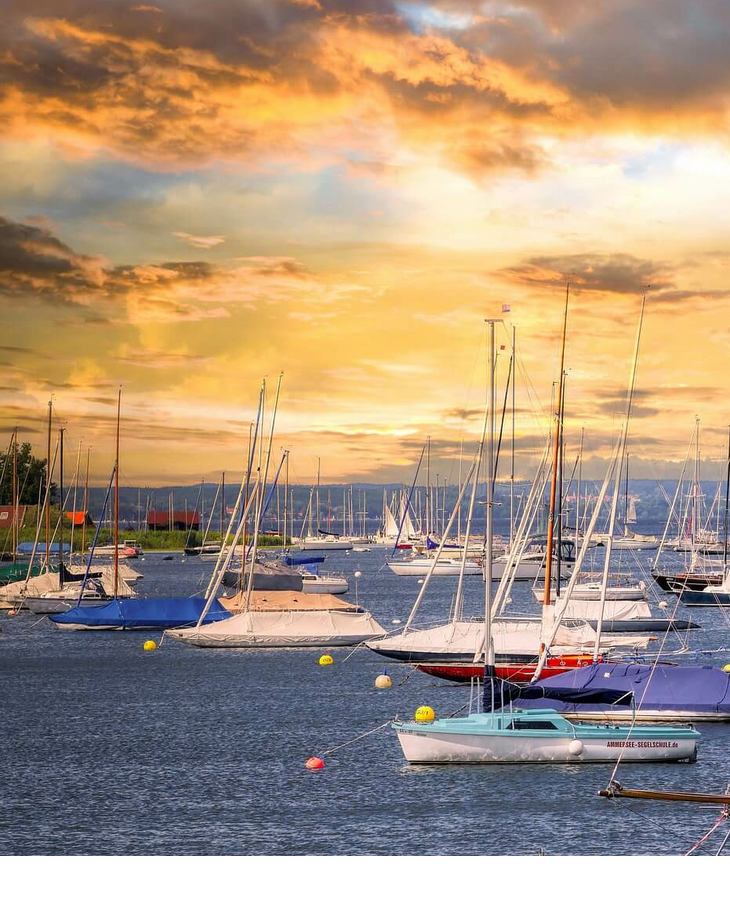 Segelboote im Hafen bei Sonnenuntergang, umgeben von ruhigem Wasser und einem dramatischen Himmel.