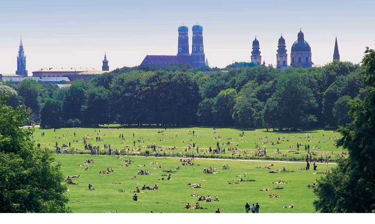 Großer Park mit vielen Menschen auf einer Wiese, im Hintergrund historische Gebäude und Kirchtürme.