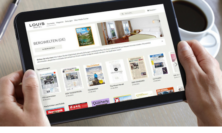 Person hält ein Tablet mit einer Hotelwebseite, daneben eine Tasse Kaffee auf einem Tisch.