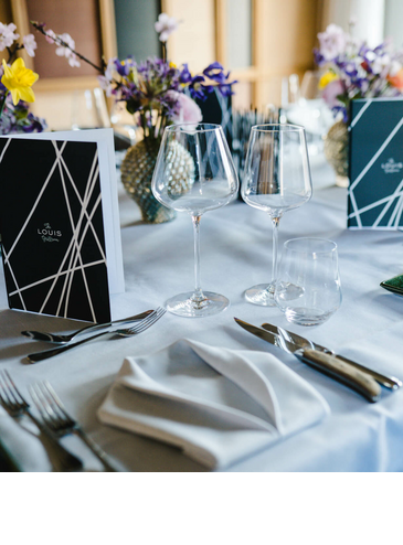 Elegante Tischdekoration im LOUIS Hotel München mit Blumen, Gläsern und stilvollen Menükarten.