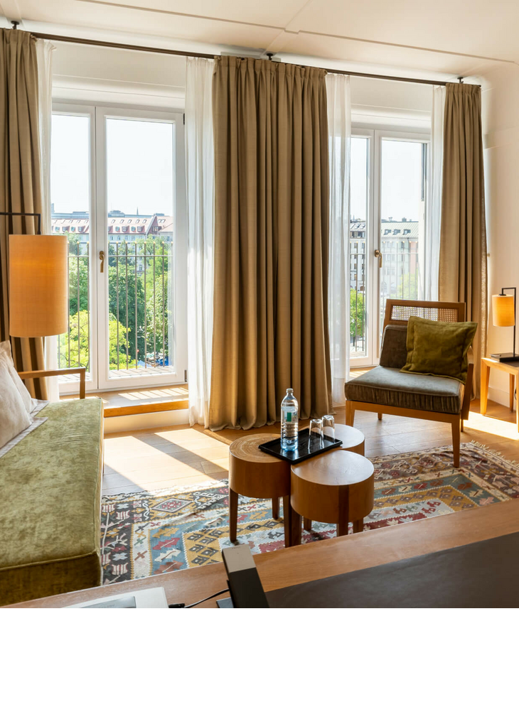 Helles Hotelzimmer mit modernen Möbeln, großen Fenstern und Blick auf die Stadt im LOUIS Hotel München.