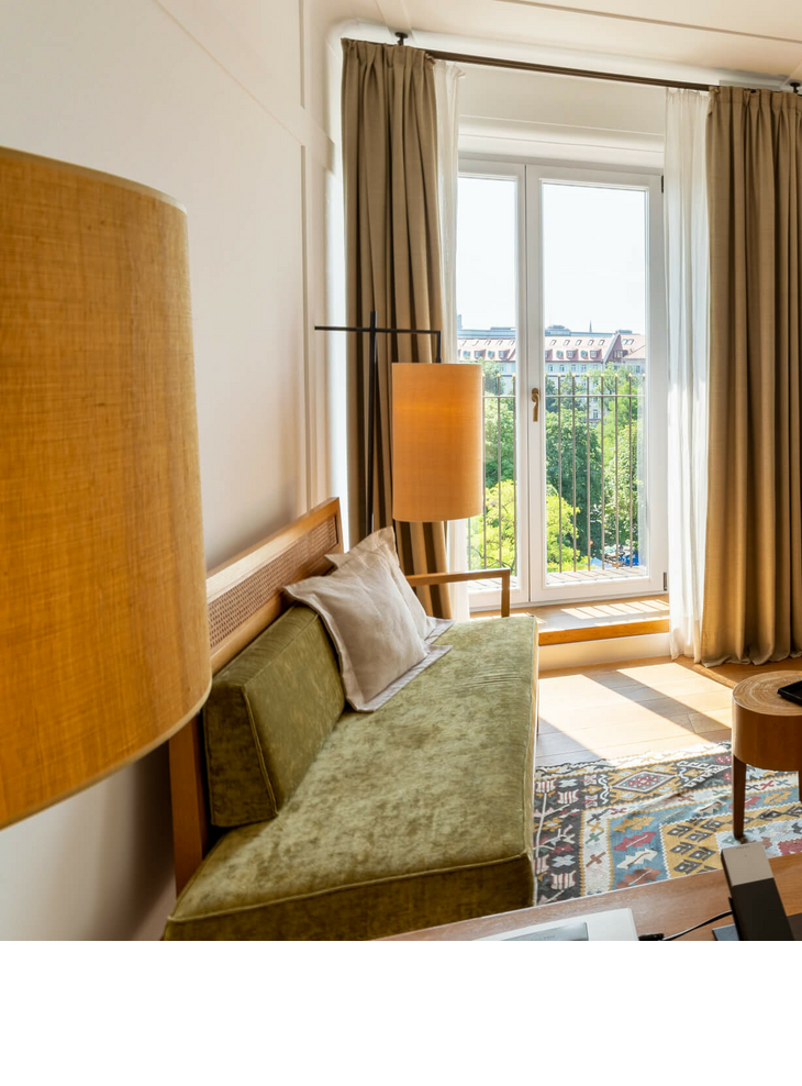 Helles Hotelzimmer mit modernen Möbeln, großen Fenstern und Blick auf die Stadt im LOUIS Hotel München.