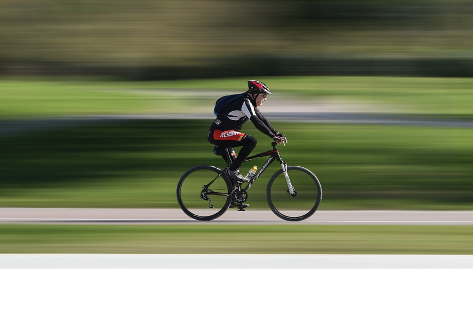 Radfahrer mit rotem Helm fährt schnell auf einem Radweg durch einen grünen Park.