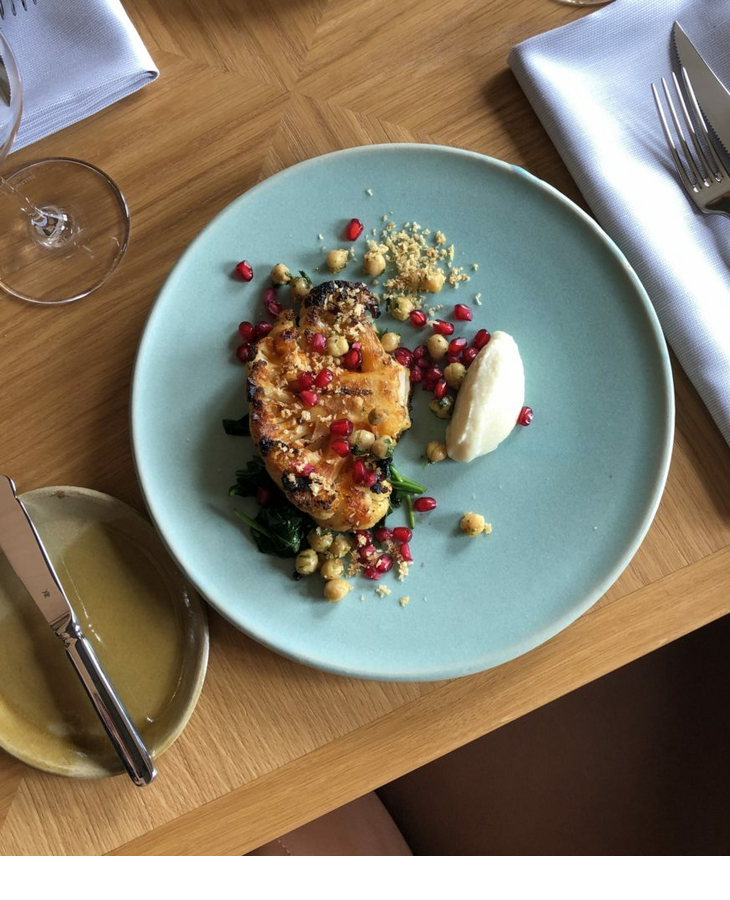 Elegantes Gericht mit gegrilltem Gemüse, Kichererbsen, Granatapfelkernen und Creme auf blauem Teller im LOUIS Hotel.
