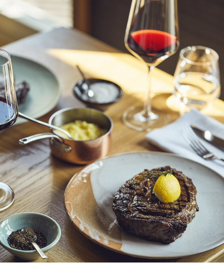 Steak mit Zitrone, Rotweinglas, Kartoffelpüree und Gewürzen auf Holztisch im LOUIS Hotel München.
