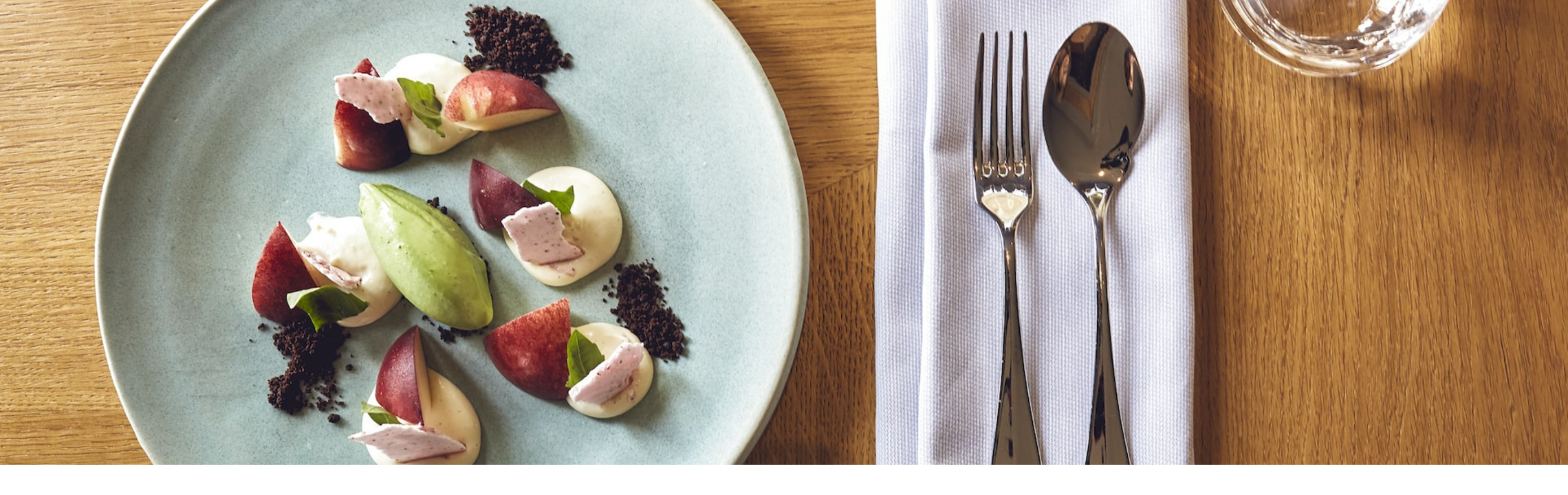 Elegantes Dessert auf blauem Teller mit Besteck und Gläsern auf Holztisch im LOUIS Hotel München.