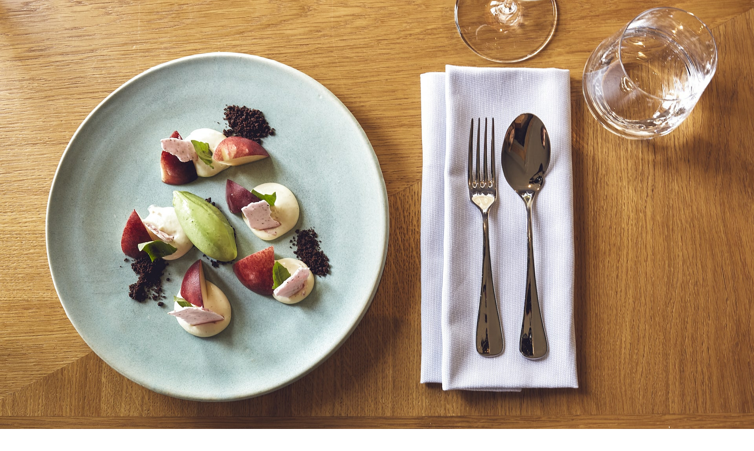 Elegantes Dessert auf blauem Teller mit Besteck und Gläsern auf Holztisch im LOUIS Hotel München.