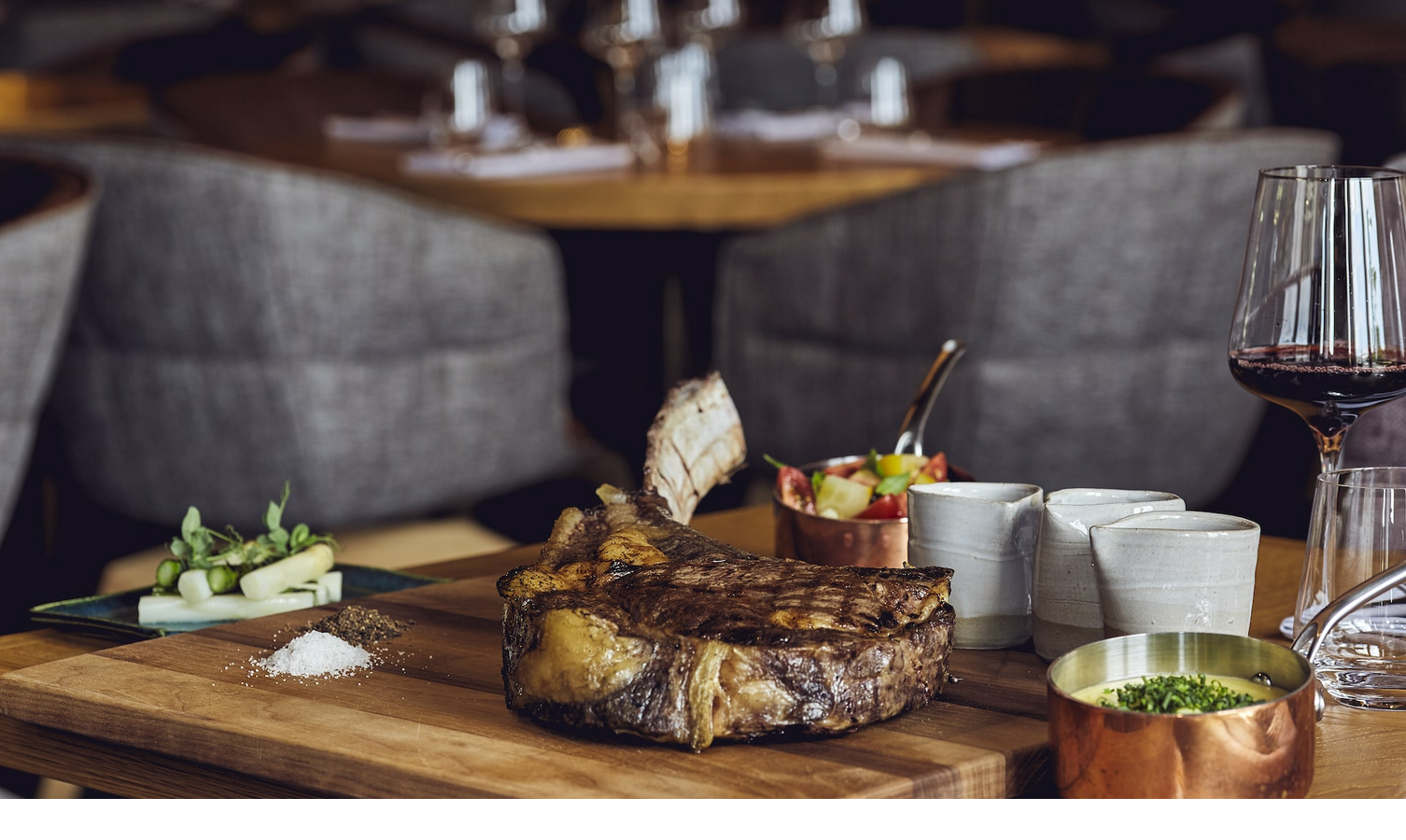 Elegantes Steakgericht mit Beilagen und Rotweinglas auf Holztisch im stilvollen Restaurant des LOUIS Hotel München.