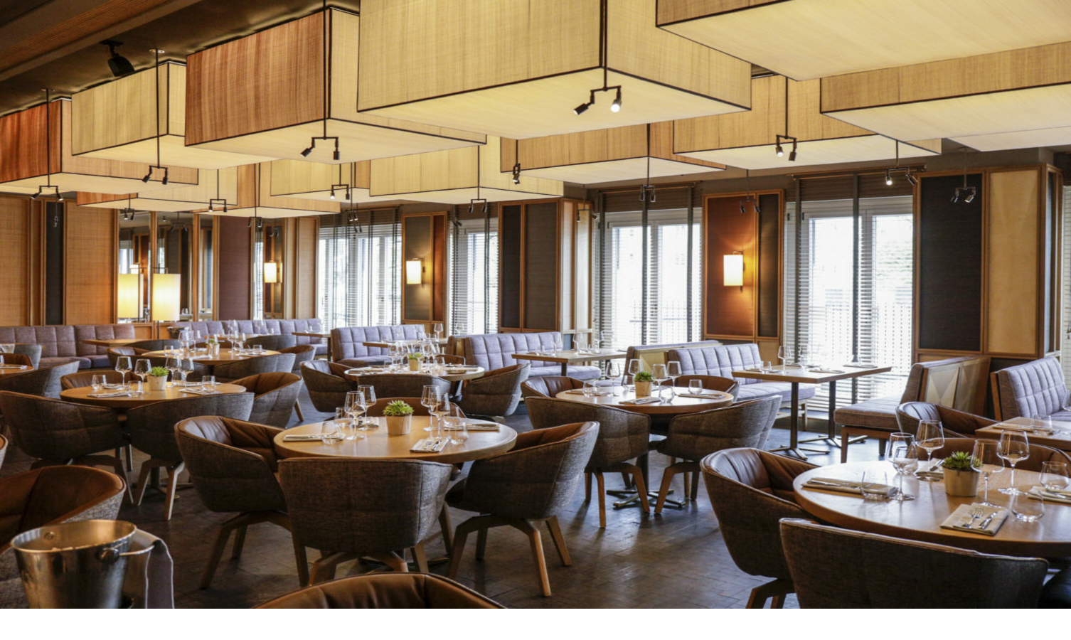 Elegantes Hotelrestaurant mit runden Holztischen, gepolsterten Stühlen und modernen Lampen, Tageslicht durch Fenster.