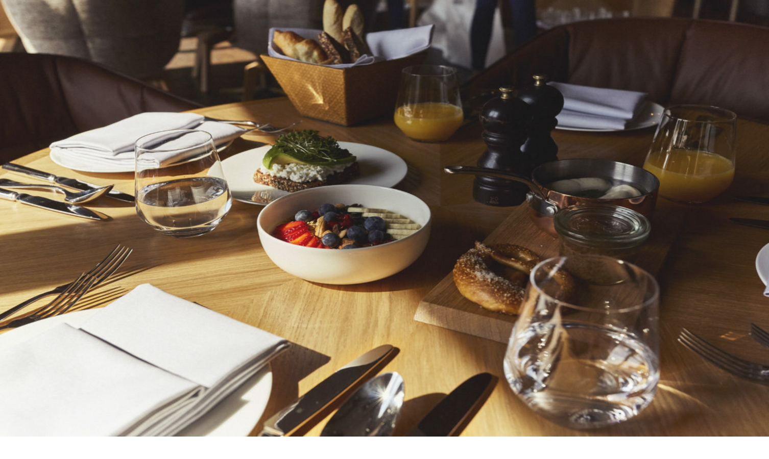 Frühstückstisch im LOUIS Hotel München mit Obstschale, Brot, Saft und Besteck auf Holztisch.